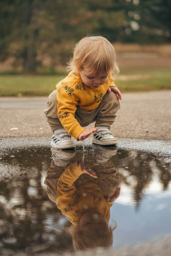 Baby playing outside in water puddle