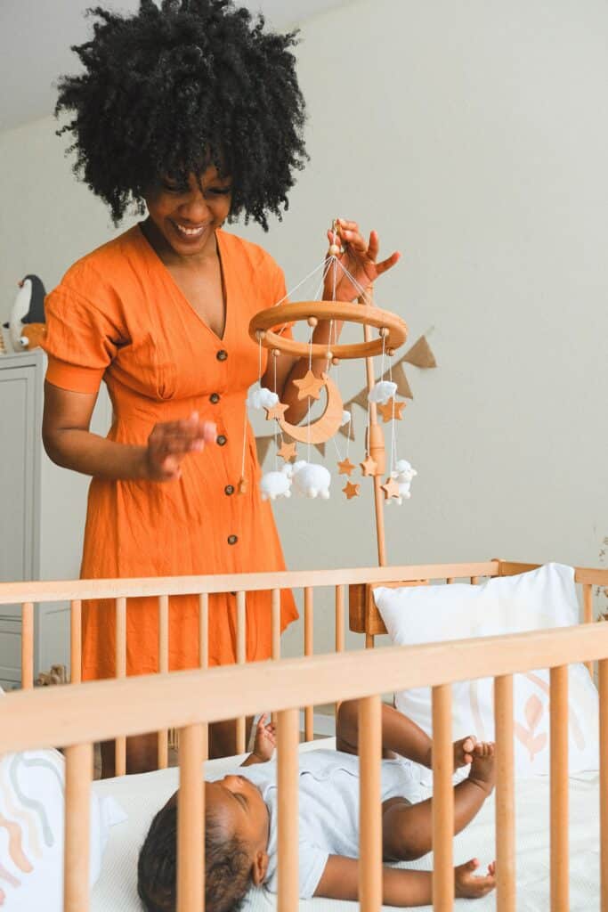 Woman adjusting mobile over baby crib