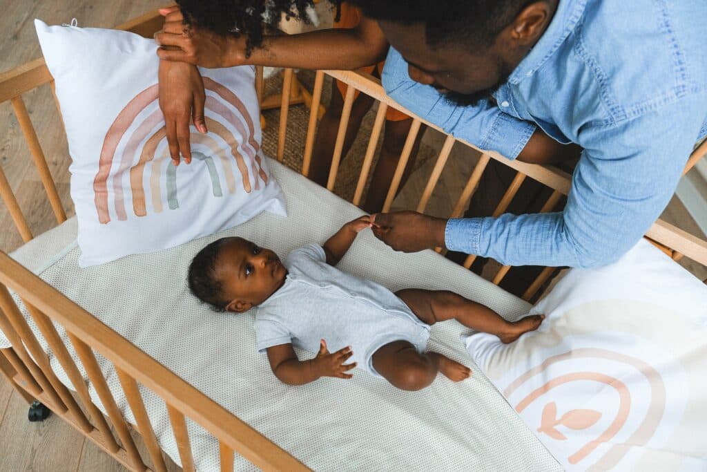 Parents looking at baby in wooden crib