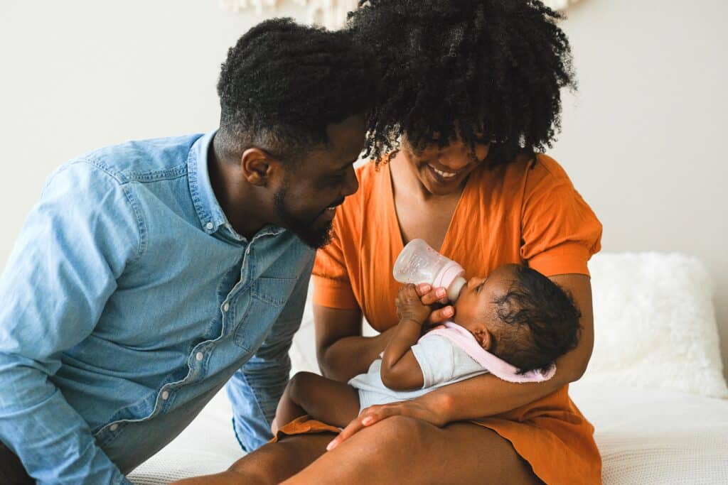 Mom and dad smiling at baby bottle feeding