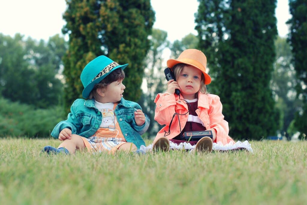 Two toddlers sitting in the grass in hats