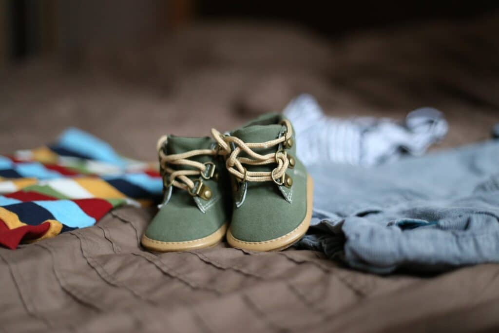 Baby shoes and clothes laying on bed