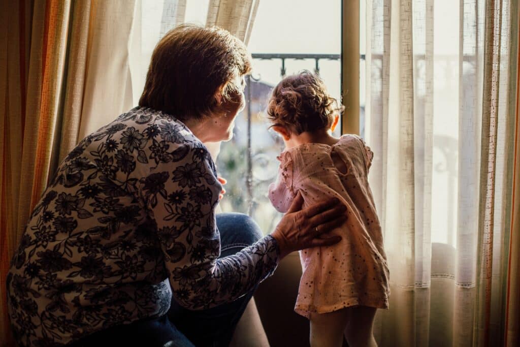 Grandmother looking out a window with her young granddaughter