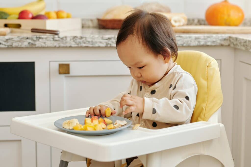 Baby eating food from plate on high chair