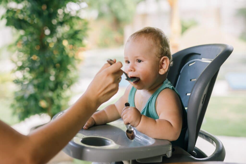 Baby eating food from a spoon in their high chair