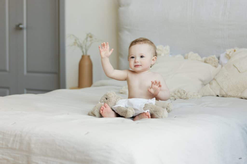 Baby sitting on bed with arm raised