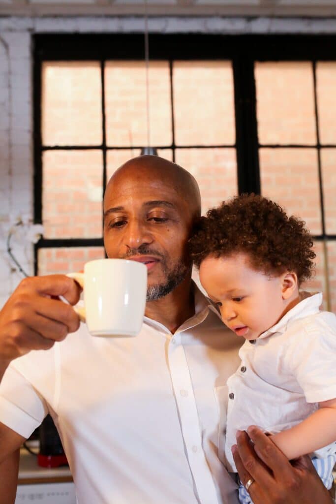 Dad drinks coffee while holding toddler
