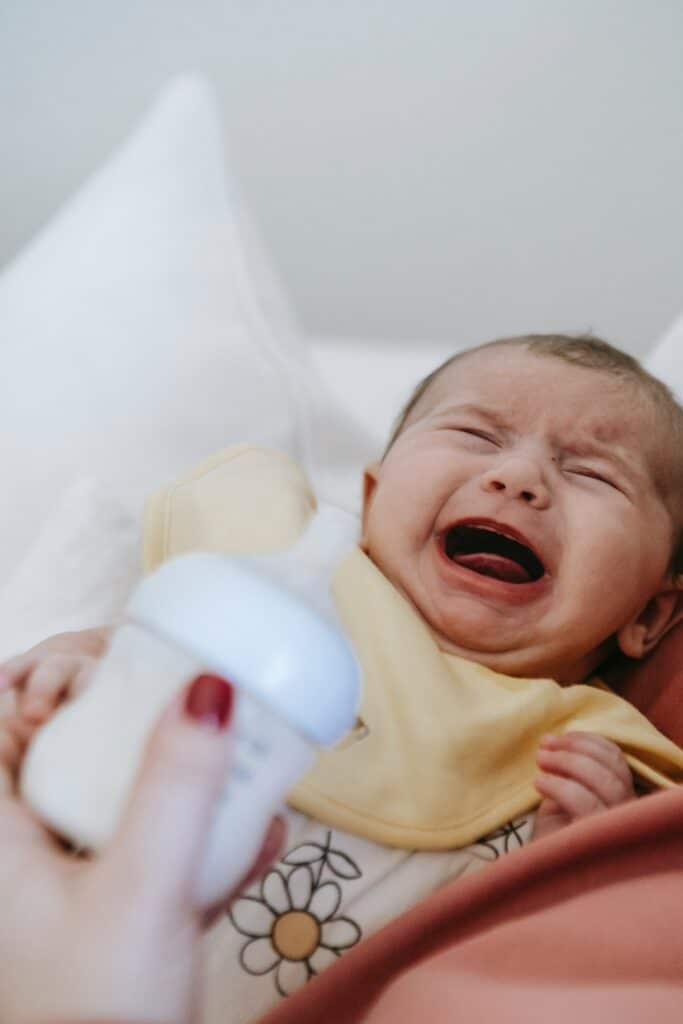 Young baby crying and rejecting a bottle of milk