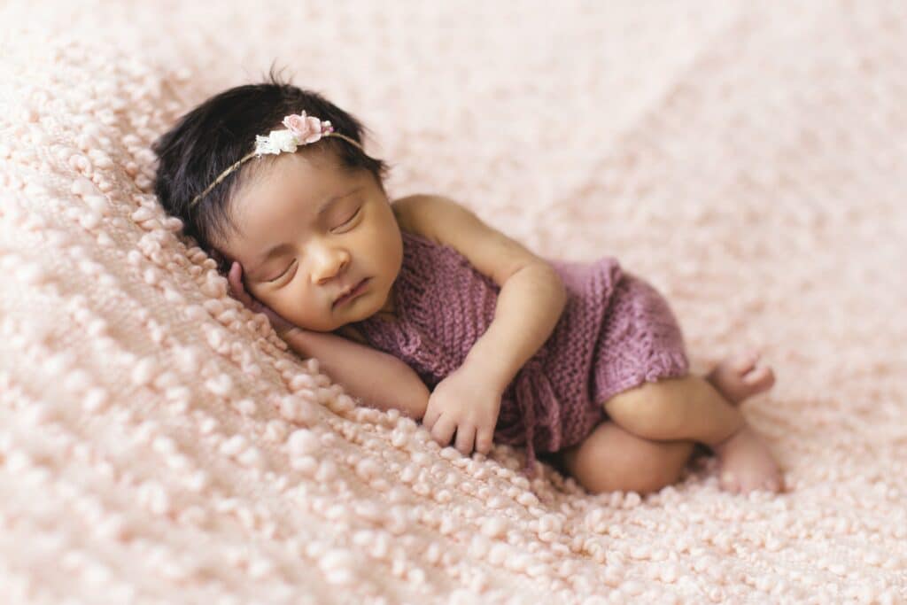 Newborn baby girl cuddled up on a pink blanket for a photo shoot