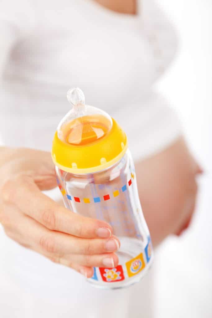 Pregnant person holding an empty baby bottle
