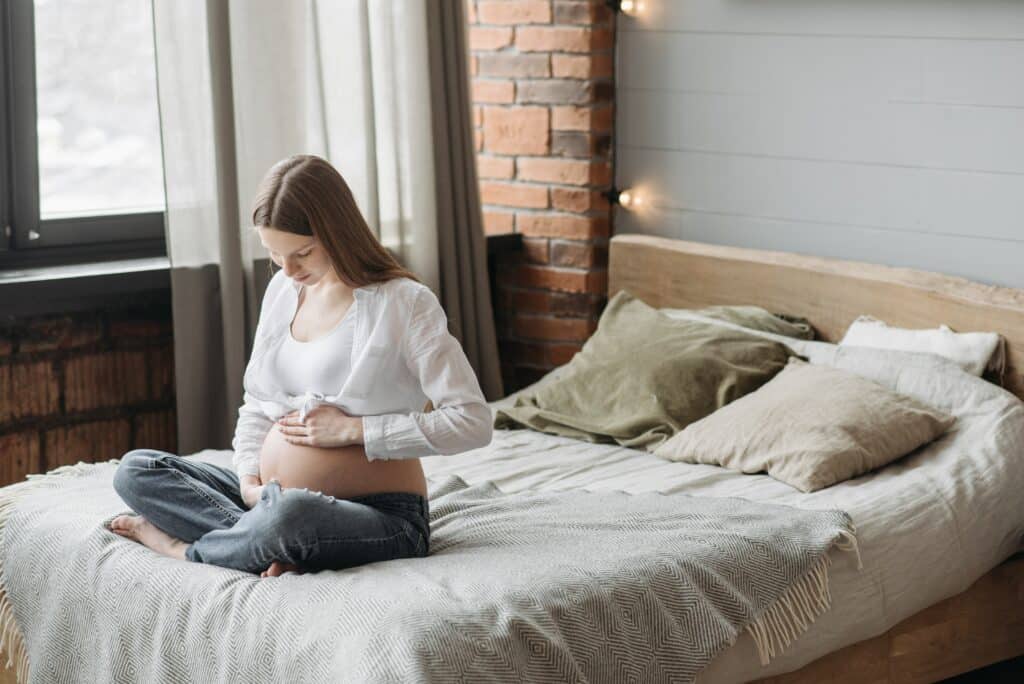 Woman holding her pregnant belly on bed