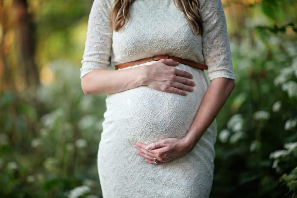 Pregnant woman holding her belly in white dress