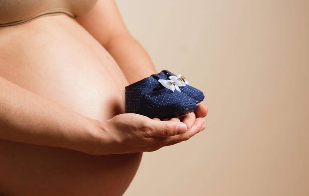 Pregnant woman belly with baby shoes